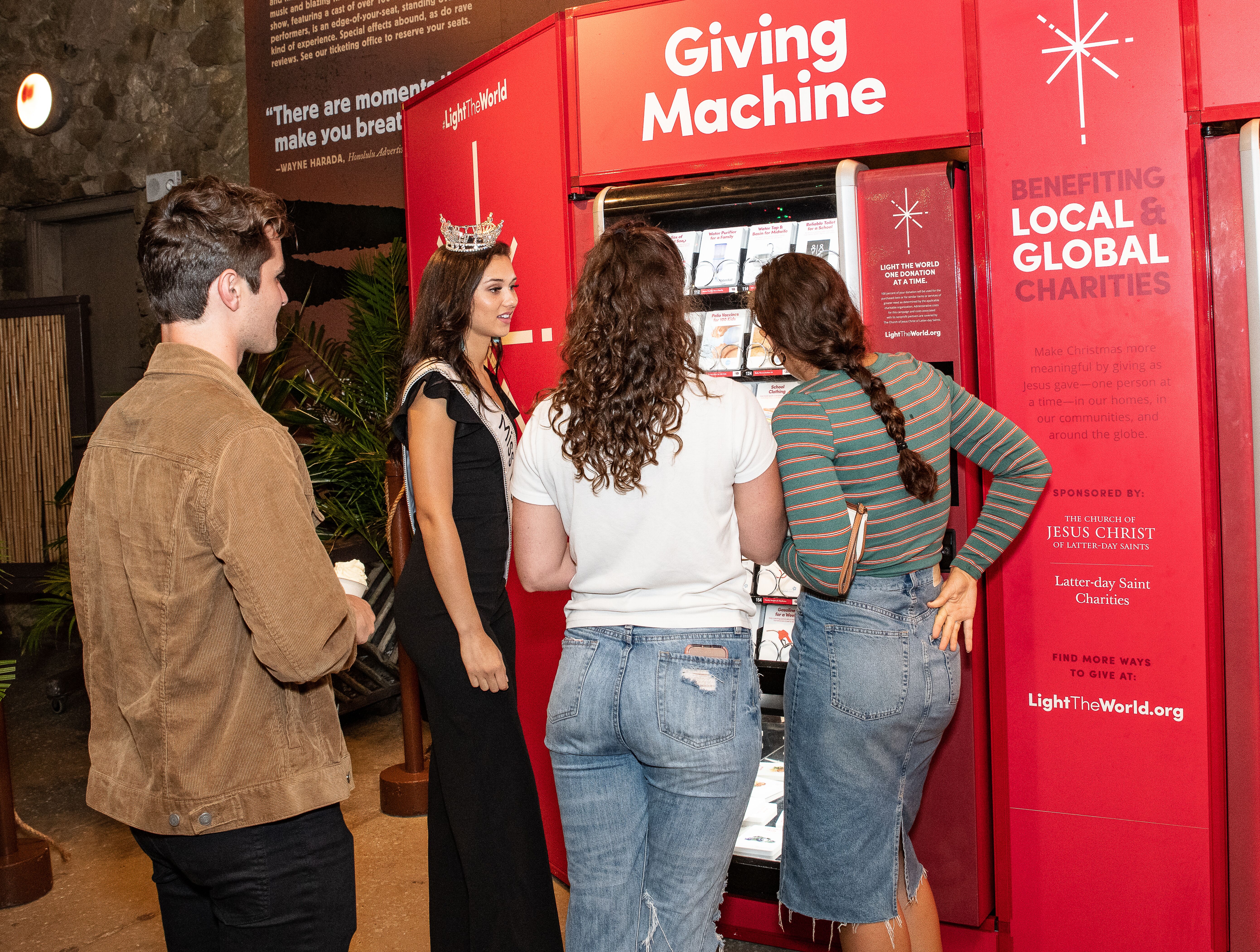 Photo of Miss Hawaii, Nikki Holbrook, helping 3 visitors to place their donation order at the Giving Machine