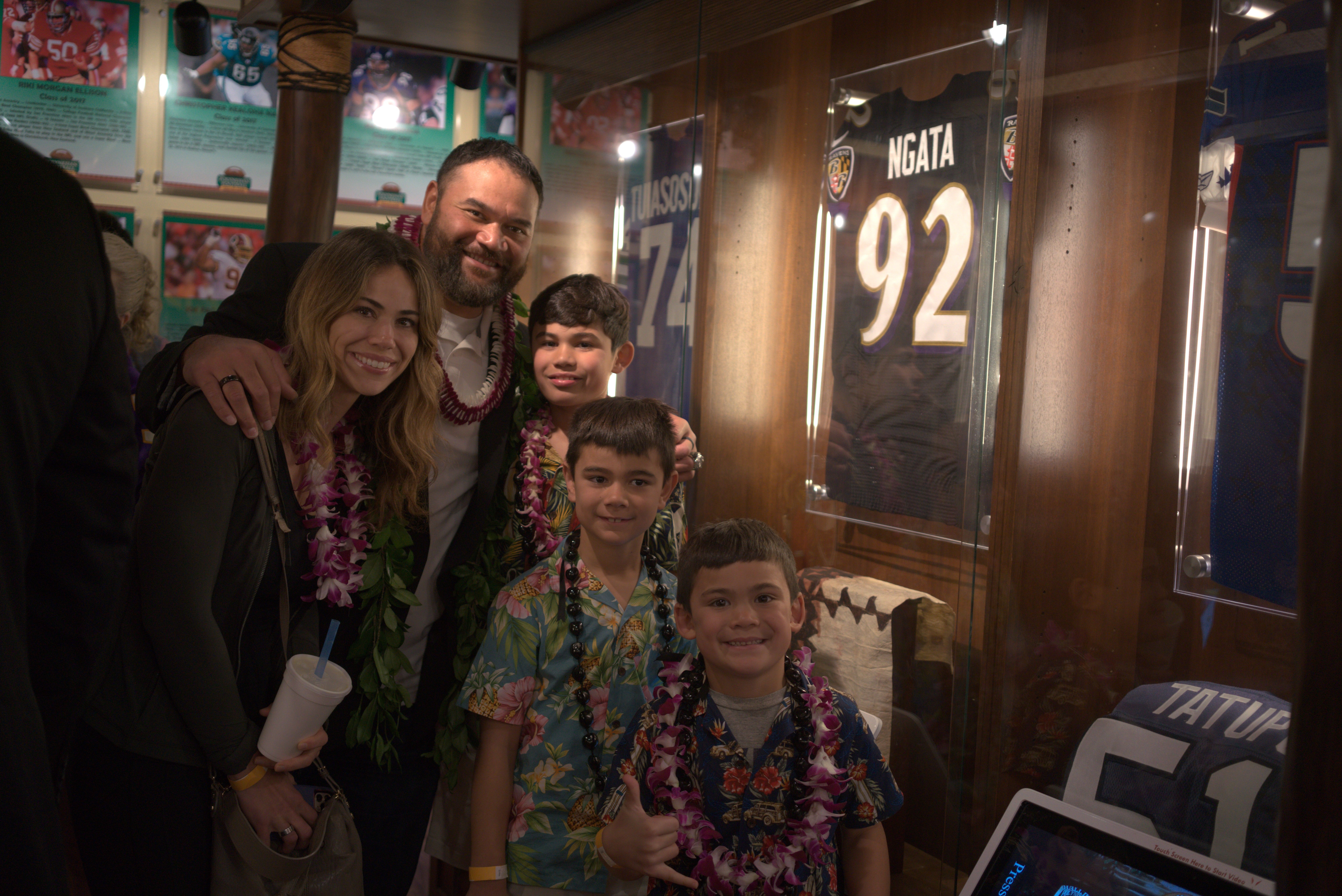 Photo of Haloti Ngata and his family stand next to his display case at the Polynesian Football Hall of Fame at the Polynesian Cultural Center during the induction ceremony festivities.