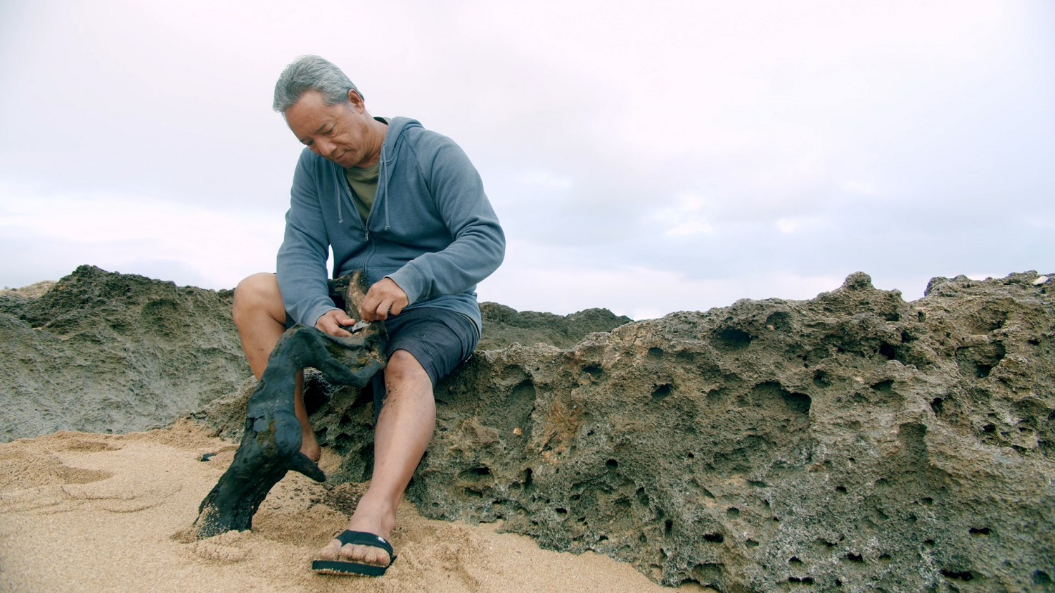 Photo of Kawika Eskaran as he works with a branch by the sea