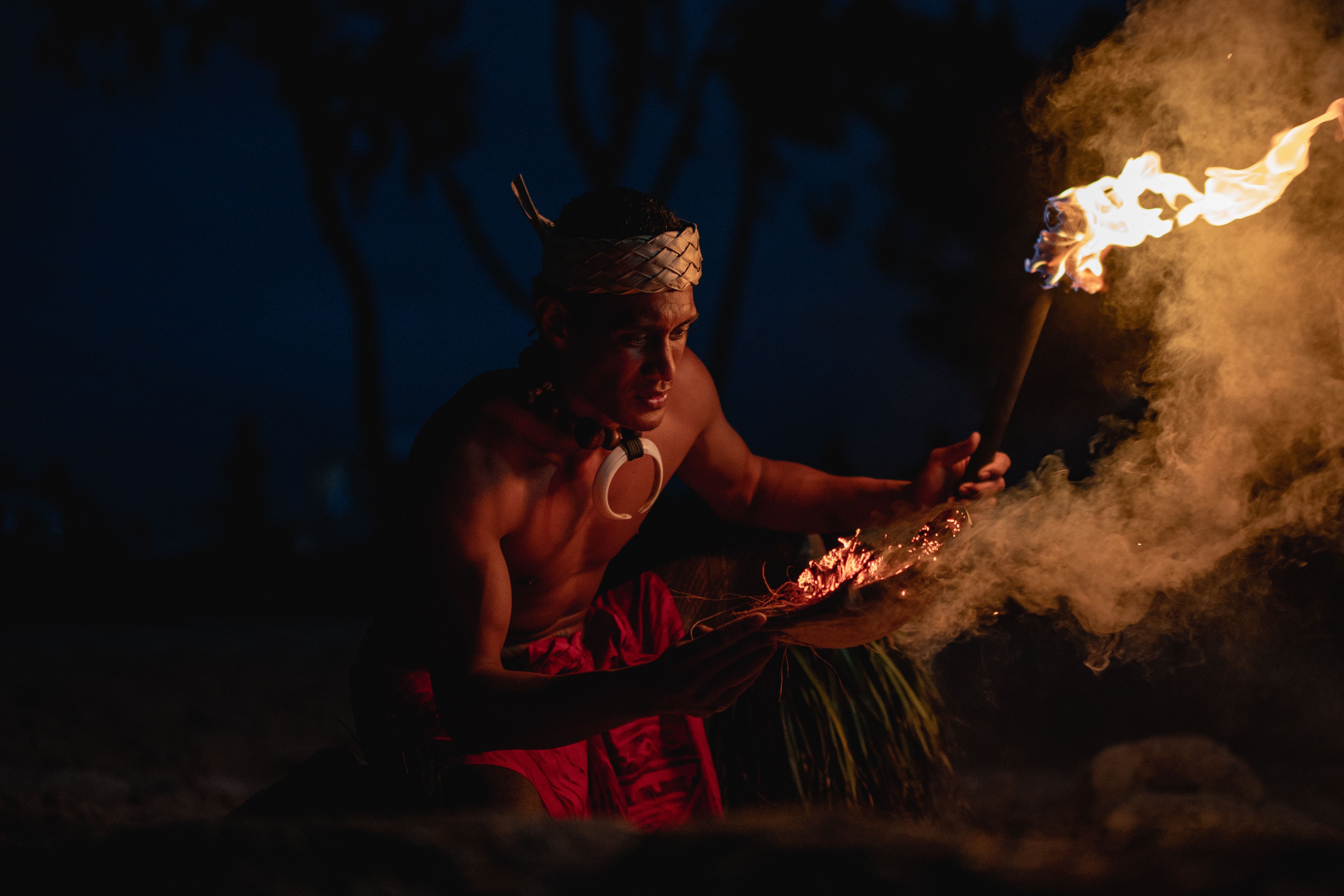 A Samoan male fireknife dancer is showing how he lights his war knife (nifo oti) using fire and coconut husk