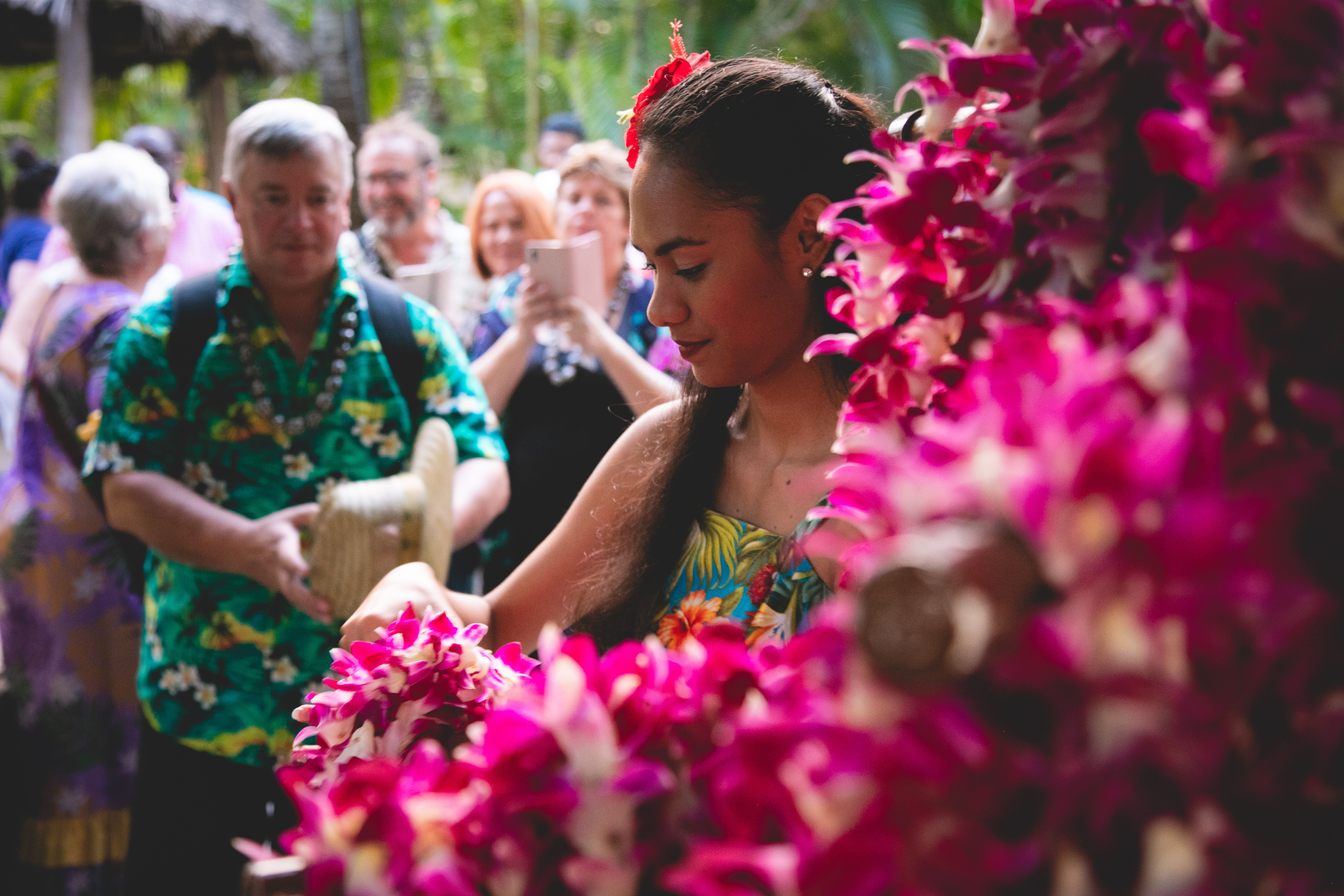 a beautiful Polynesian lady greeting and welcoming the guests with fresh flower leis to the front entrance of Hale Aloha at the Polynesian Cultural Center