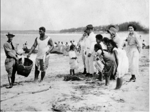 black and white photo of men, women, and children at the Hukilau Beach, Oahu.