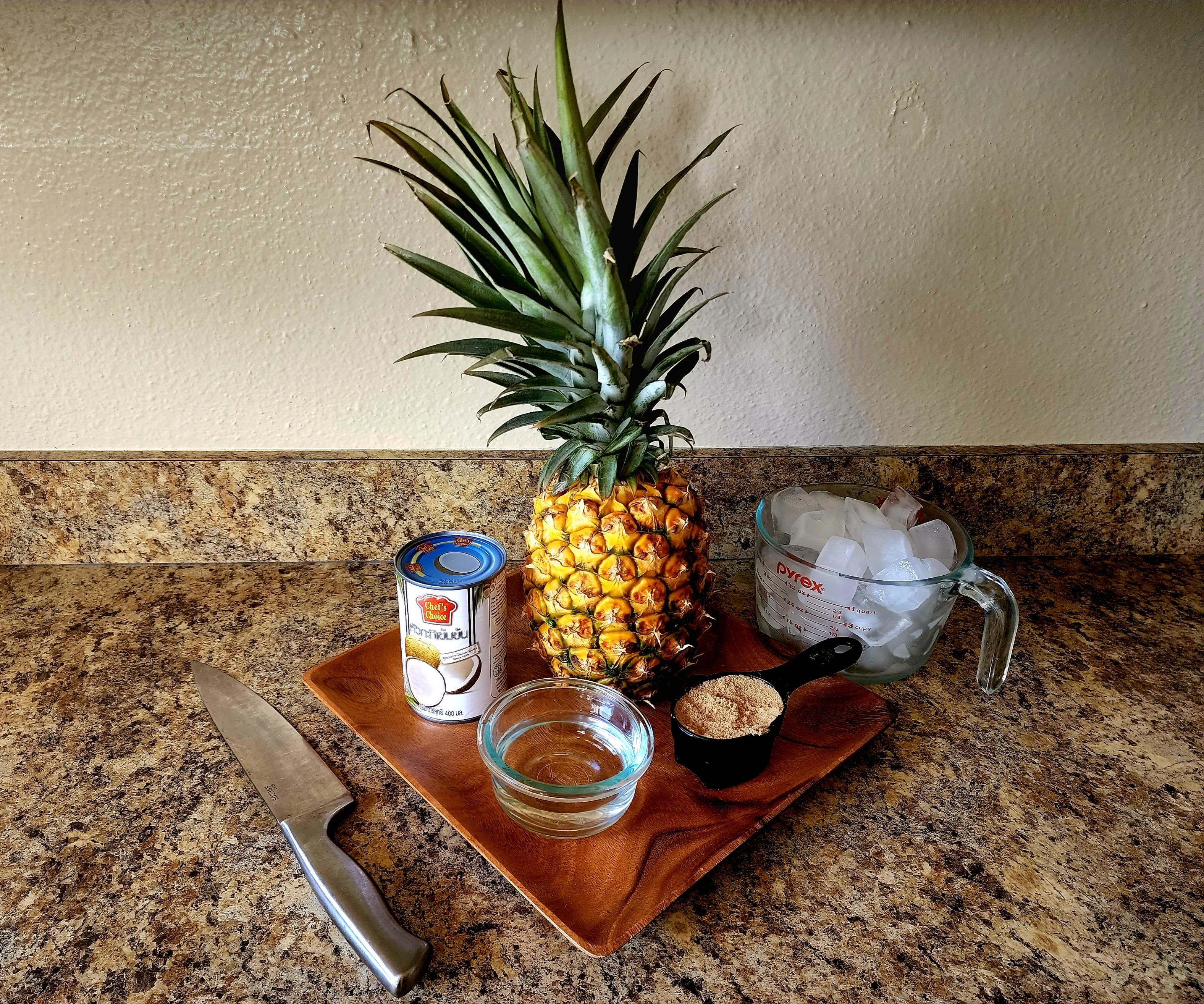photo of ingredients to make vaifala Samoa. Ingredients include a 1/2 cup of water, 1/2 cup of sugar, 1 can of coconut cream, 1 whole pineapple and ice blocks.