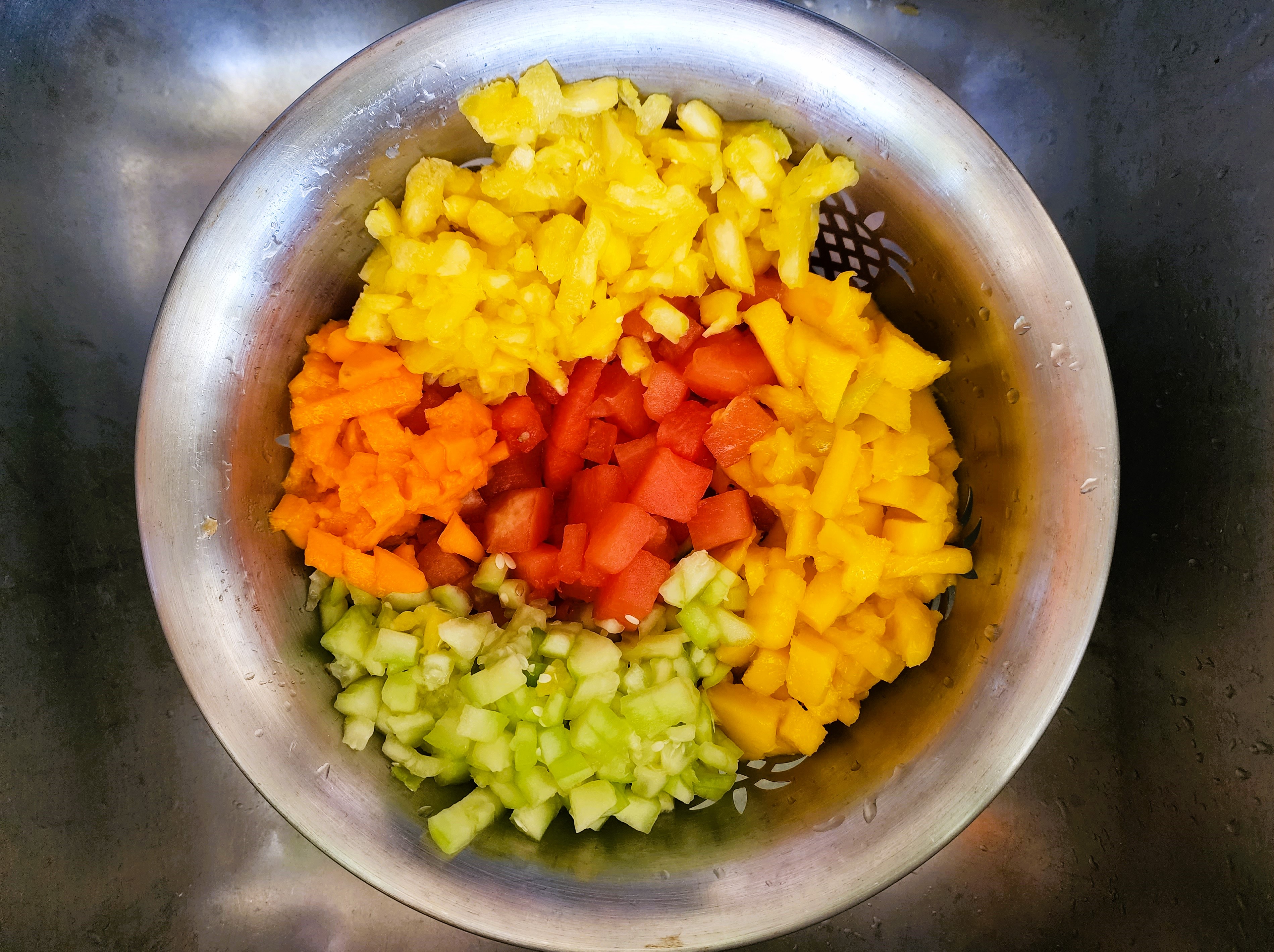 Image of chopped pineapple, papaya, mango, cucumber and watermelon in a strainer