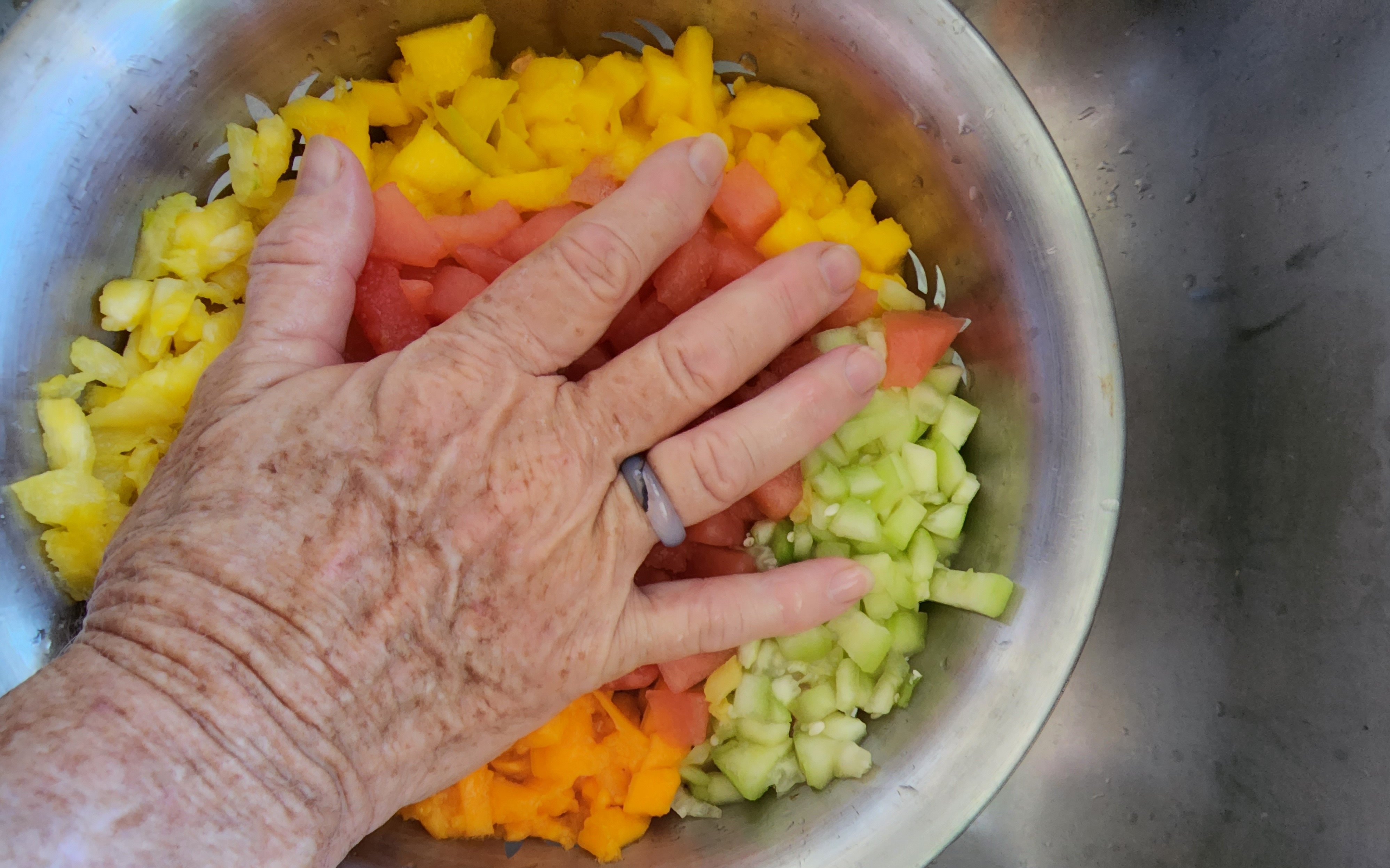 image of hand on top of chopped fruits and vegetables in a strainer sitting in a sink