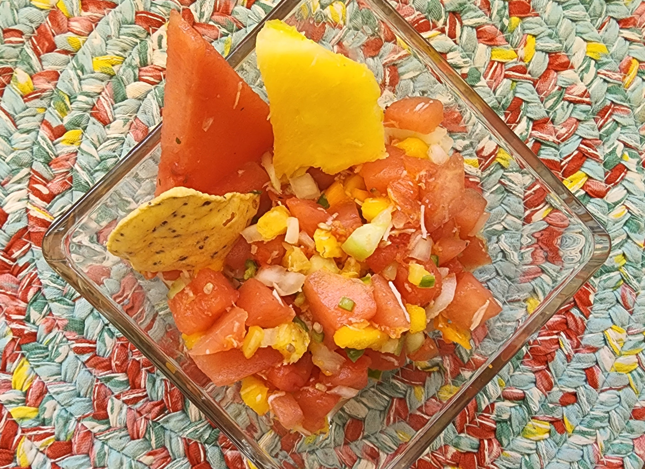 image of a small bowl of tropical fruis salsa with a slice of pineapple, a slice of watermelon and a tortilla chip