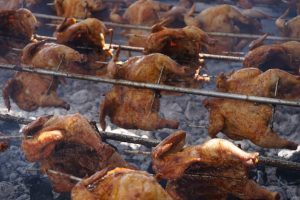 traditional method of grilling whole chickens to make huli huli chicken