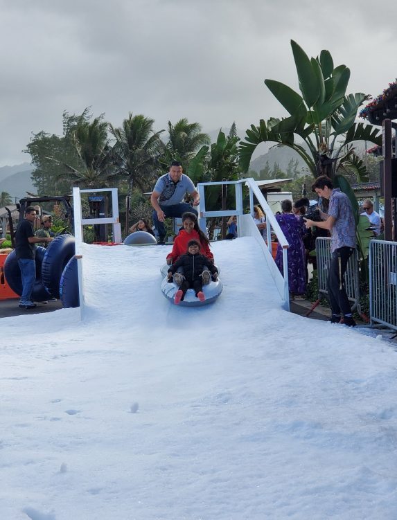 A photo of a father and his two kids enjoying the Snow Day Christmas celebration at the Hukilau Marketplace