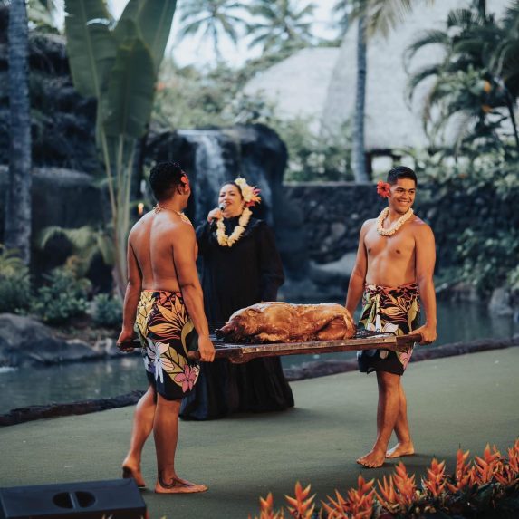 image of Mistress of Ceremonies and two Polynesian servers carrying a roasted pig