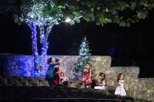 image of six young girls and kupuna (old auntie) sitting in front of the big and small Christmas trees