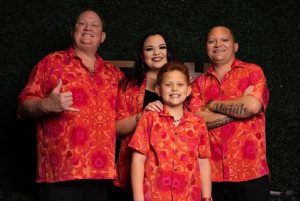 photo of two men, one woman and a pre-teen boy in red aloha shirts with black background