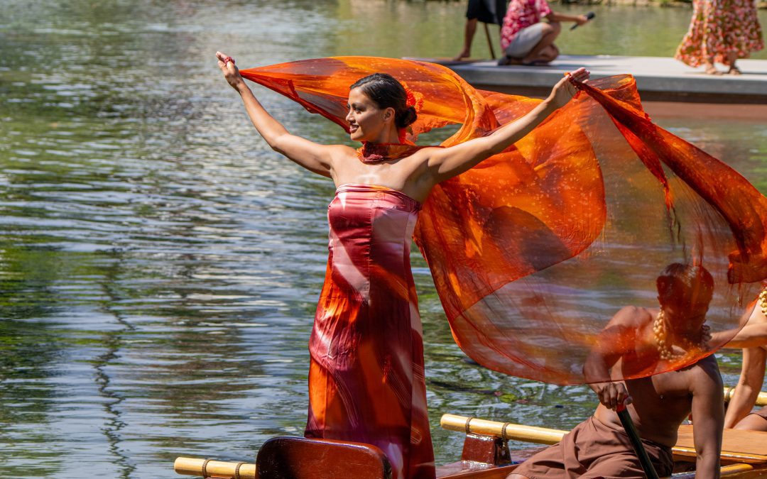 A lady in a flowy red and orange costume on a canoe.