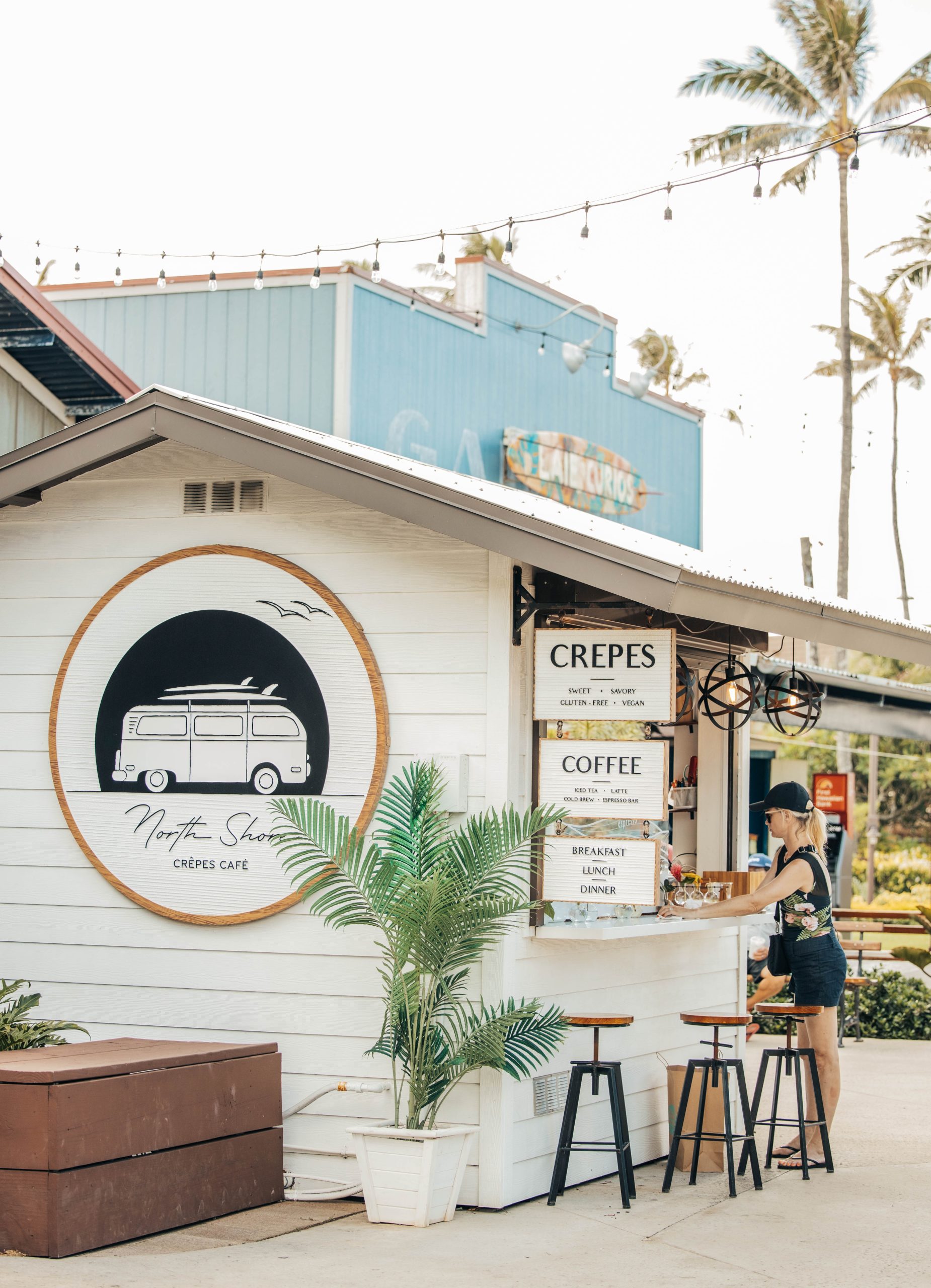 The side of North Shore Crepes. A white wood wall with a circular logo that features a beach bus