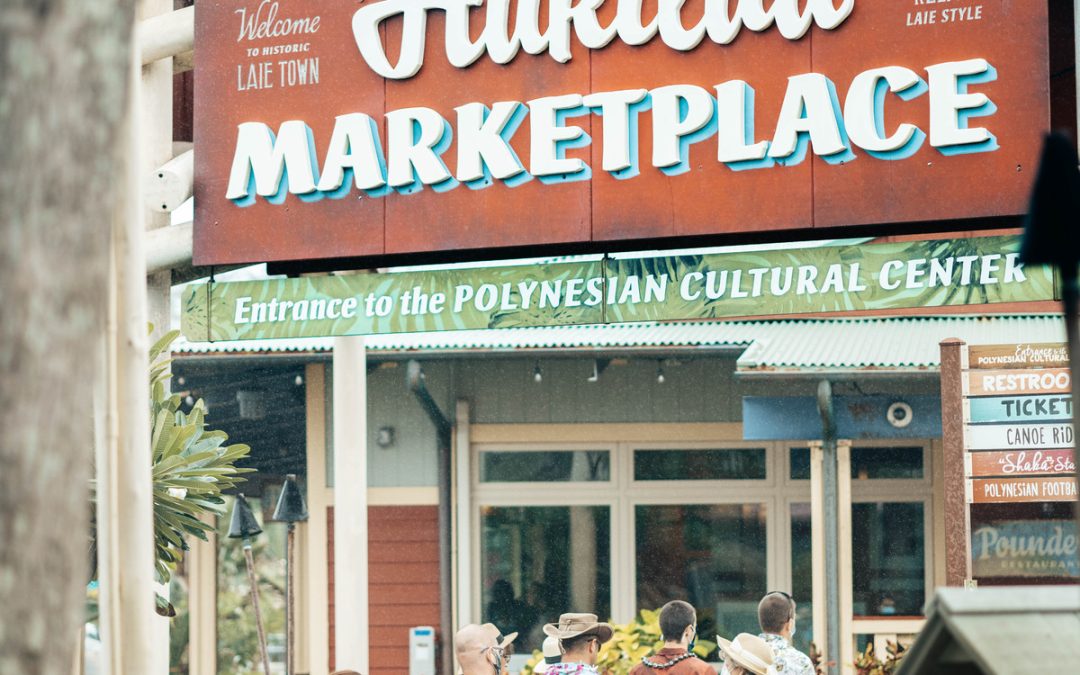 A group of people walking through the red gateway into the Hukilau Marketplace