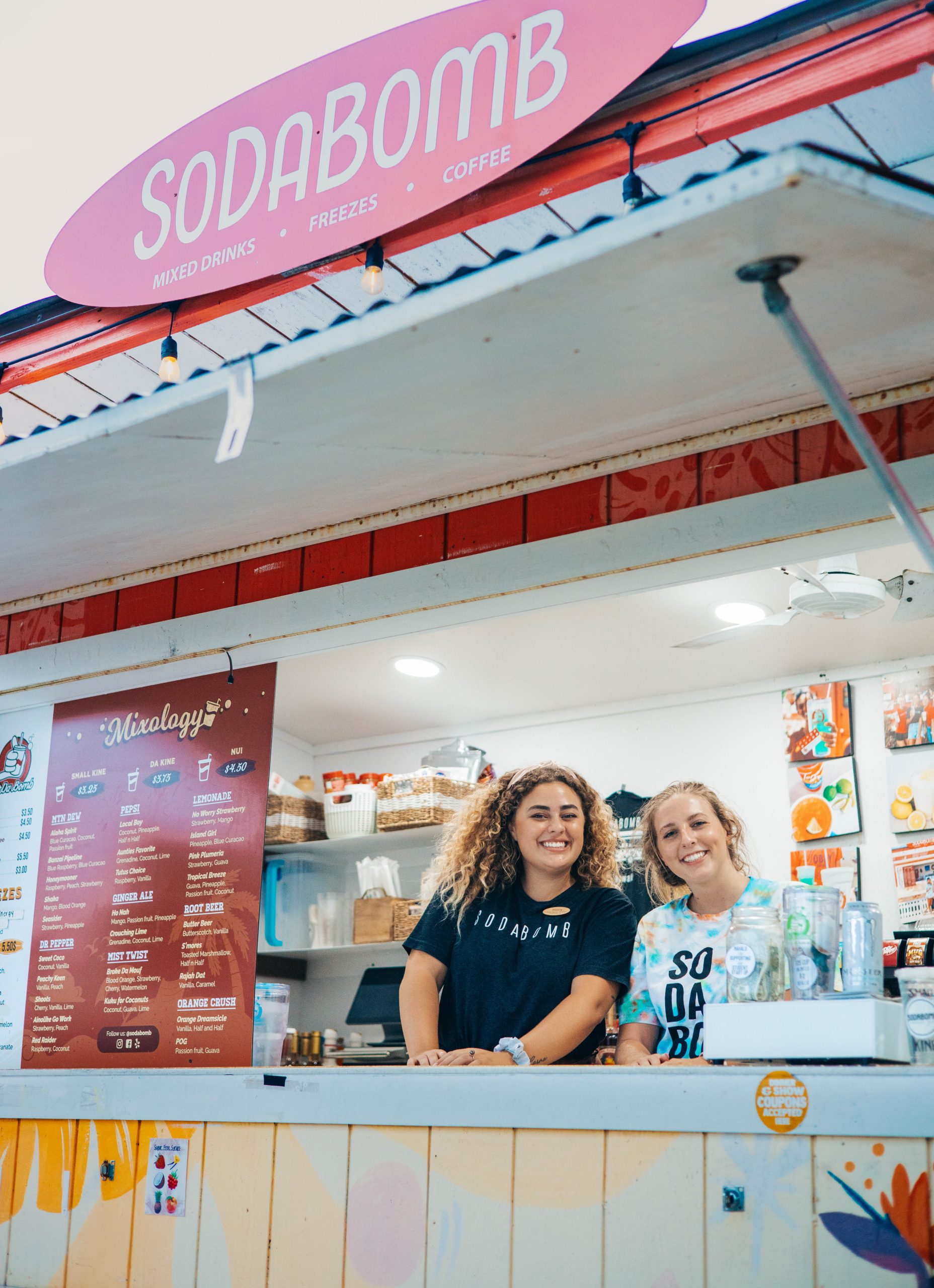 Two smiling employee in the window of So'Da Bomb's storefront