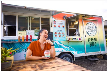 Woman in rust-colored top in front of rainbow-colored food truck