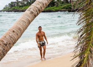 Man in swim trunks, smiling, walking up the beach from the ocean