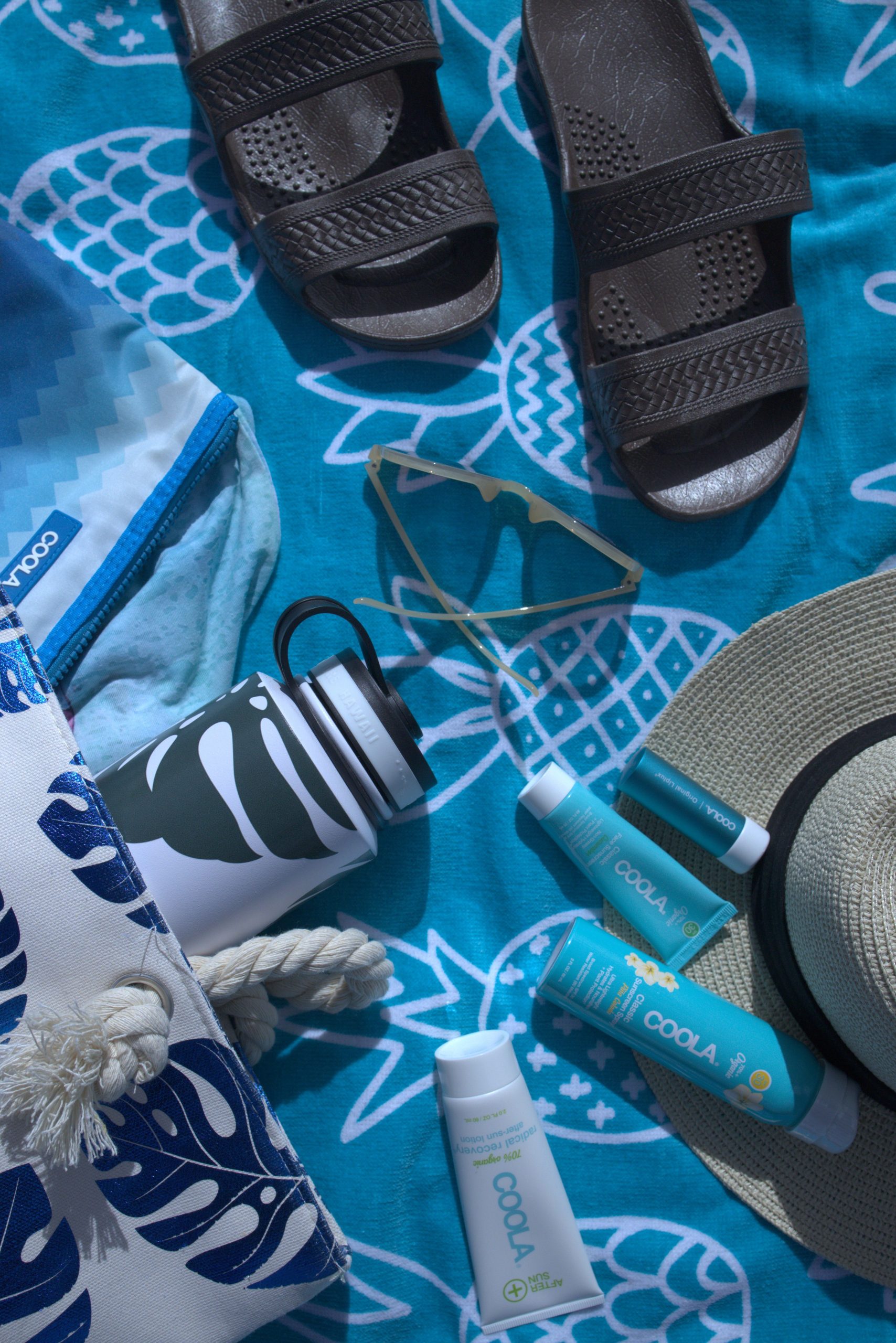 Items on a beach towel: sandals, water bottle, suncreen products