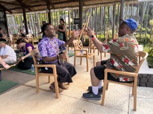 A guide, in a purple shirt and sulu, tosses sticks back and forth with a man in a flowered shirt and shorts.
