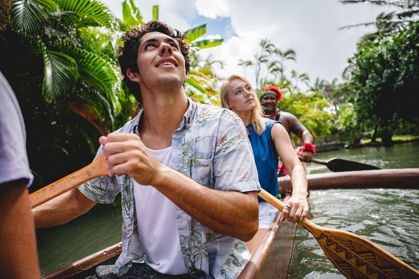 Male and female paddling a canoe with worker in costume behind them.