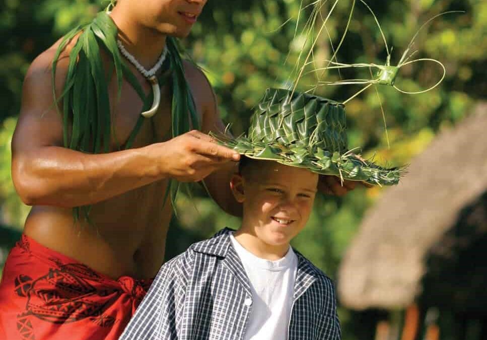 Samoan host places coconut leaf hat on young guest
