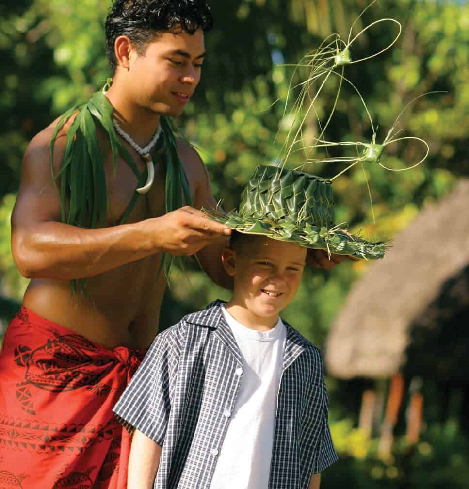 Samoan host places coconut leaf hat on young guest