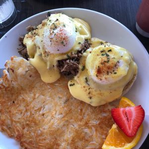 A breakfast plate of hashed potatoes and eggs with fruits on the side.