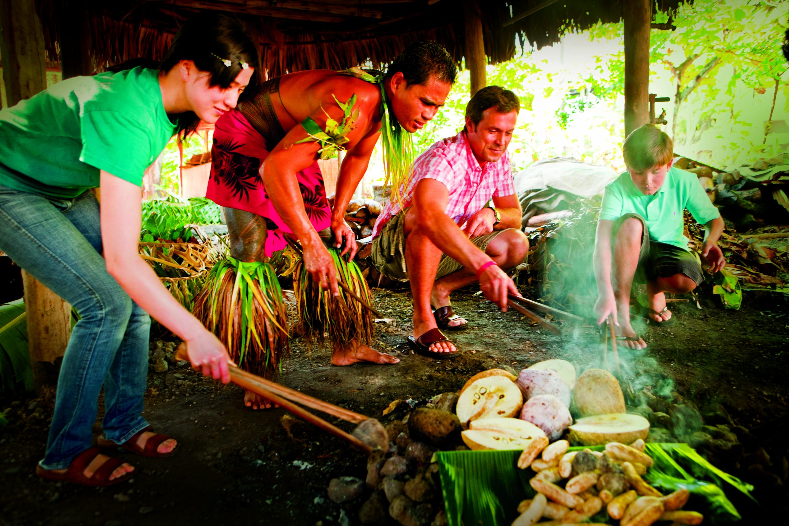 Girl, man, and boy crouch around a fire with Samoan demonstrator, cooking the island way.