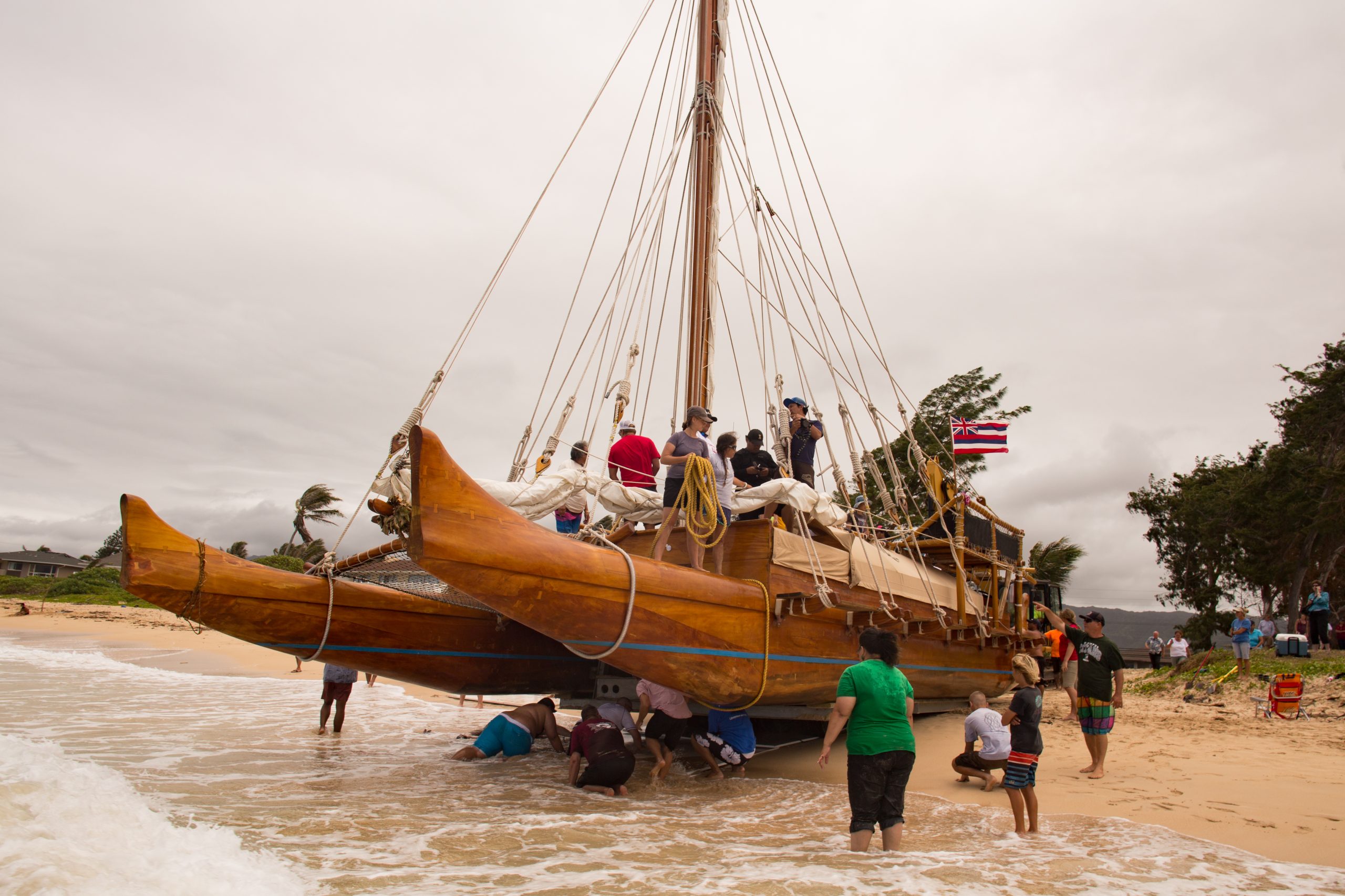 People gathered around the double-hulled canoe as they prepare to put him in the water