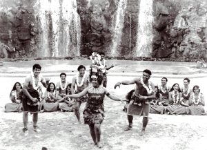 Male and female dancers in Tongan dress, performing in front of a waterfall